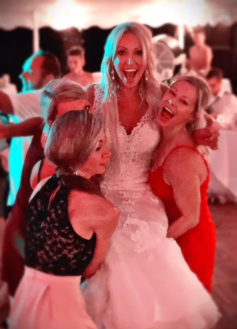 Jen laughing with friends on the wedding dance floor under red tent lighting